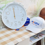 White clock with gold numbers, Pkcell branded cap, and batteries on a checkered tablecloth.