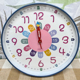 Colorful children's clock with a white face and blue rim on a patterned background Educational clock with colorful hands and numbers on a white background time teacher 300mm wide