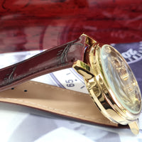 Gold watch with a brown leather strap on a white surface