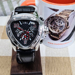 Luxury watch with black strap and detailed face, displayed on a wooden stand with a promotional leaflet in the background.