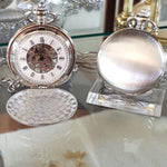 Two silver pocket watches on a reflective surface