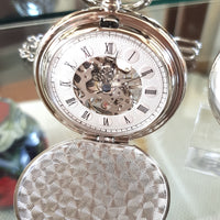 Silver pocket watch with open face showing mechanical components on a reflective surface.
