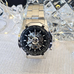 Luxury watch with a black face and silver case on a textured surface with crystal background