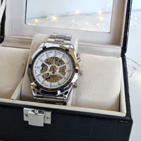 Silver wristwatch with a white face in an open jewelry box.