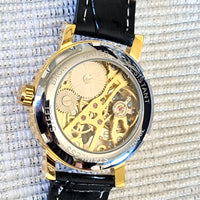 Gold mechanical watch with black strap on a textured white background