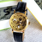 Gold mechanical watch with black leather strap on a reflective surface