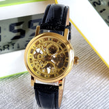 Gold mechanical watch with black leather strap on a reflective surface