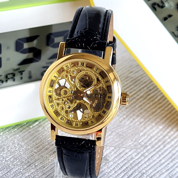 Gold mechanical watch with black leather strap on a reflective surface