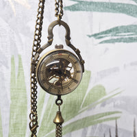 Vintage-style pocket watch with chain against a leafy background