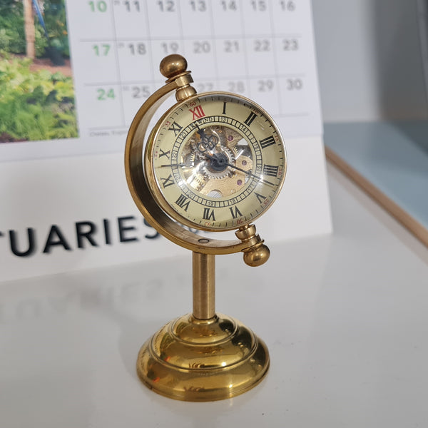 Gold decorative clock on a stand with a calendar in the background