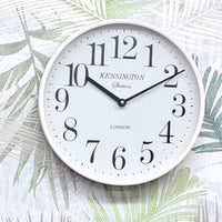 White wall clock with black numbers and text on a light background with leaf patterns