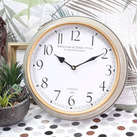 Decorative wall clock with gold rim and white face on a polka dot surface with plants.