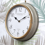 Wall clock with gold rim and white face on a leafy background