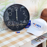 Black wall clock on a table with a white cap and batteries in the background, black with silver numbers super modern