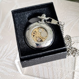 Silver pocket watch with intricate design in a black box on a textured white surface