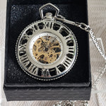 Silver pocket watch with intricate design on a black cushioned base