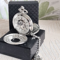 Silver pocket watch with chain on a black textured box against a light background