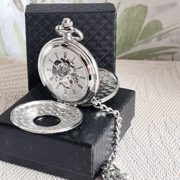 Silver pocket watch with chain on a black textured box against a light background