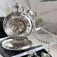 Silver pocket watch with intricate design on a reflective surface