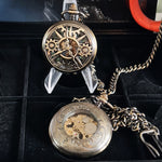 Two ornate pocket watches on a black surface with a red object in the background.