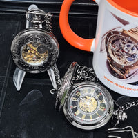 Two pocket watches on a dark surface with an orange mug featuring a watch design.