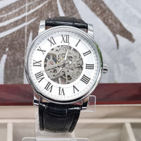 Watch with black leather strap and white face displaying Roman numerals on a stand.