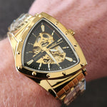 Gold wristwatch with a black face featuring a skull design on a person's wrist.